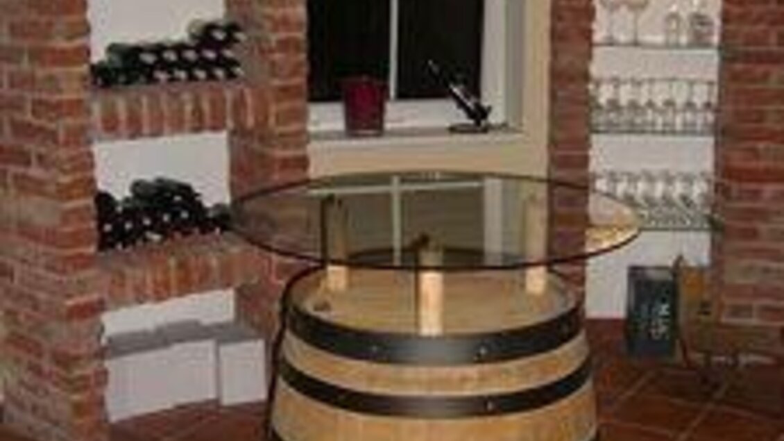 Ein gemütlicher Weinkeller mit einem Holztisch aus einem Weinfass. Regale mit Weinflaschen und Gläsern sorgen für eine einladende Atmosphäre. | © Landgasthaus Kaiser