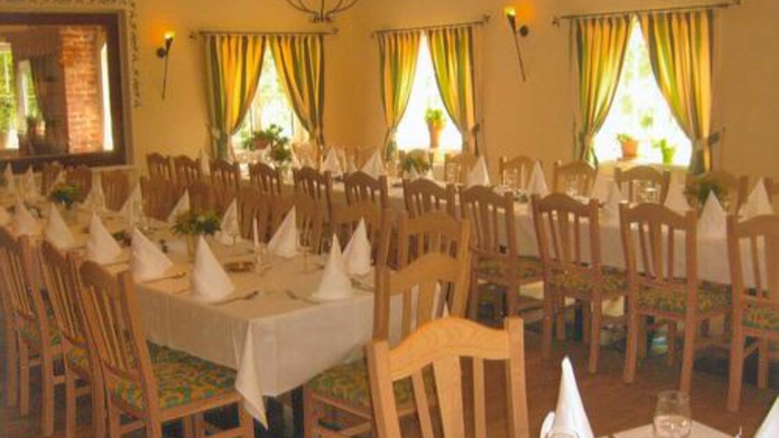 Ein einladender Restaurantbereich mit Holzstühlen und Tafeln. Die Fenster sind mit gelben Vorhängen geschmückt, und kleine Pflanzen stehen auf den Tischen. | © Landgasthaus Kaiser