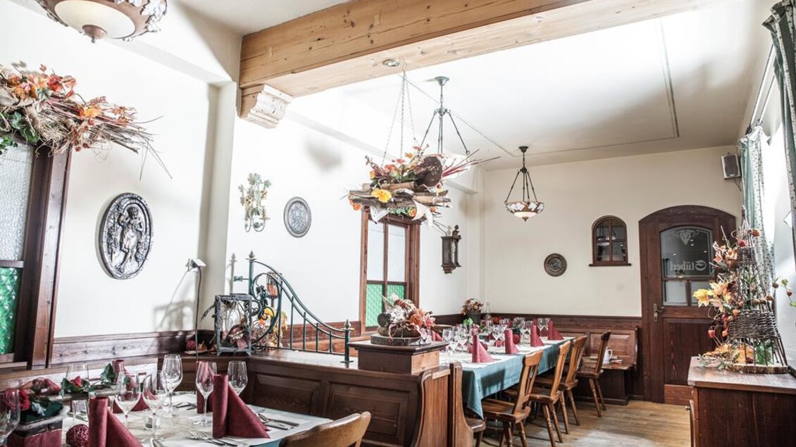 Ein gemütliches Restaurant mit Holzinterieur und festlich gedeckten Tischen. Die Wände sind mit dekorativen Elementen und Pflanzen geschmückt. | © Landgasthof Erlsbacher