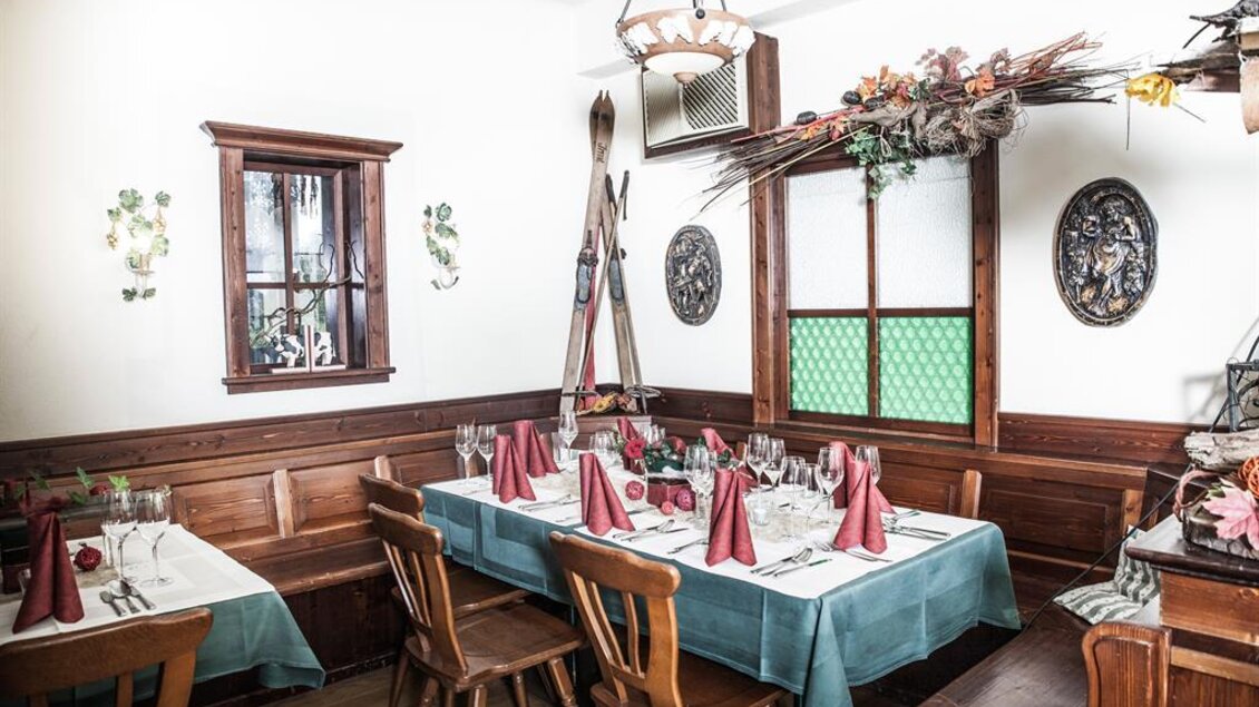 Ein einladendes Restaurant mit holzgetäfelten Wänden und rustikalen Möbeln. Der Tisch ist festlich gedeckt mit roten Servietten und Gläsern. | © Landgasthof Erlsbacher