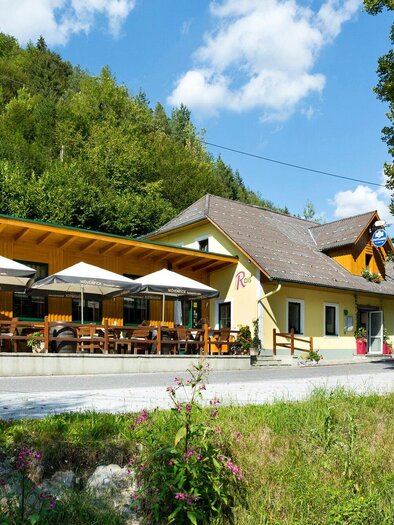 A cozy restaurant with a spacious terrace and sun umbrellas. Surrounded by green hills and a blue sky. | © TV Region Graz - Rene Vidalli