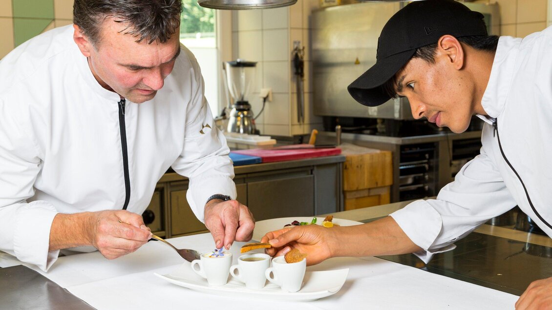 Zwei Köche arbeiten gemeinsam in einer Küche und dekorieren Teller mit kleinen Desserts und Kaffee. Sie konzentrieren sich auf die Präsentation der Speisen. | © TV Region Graz - René Vidalli