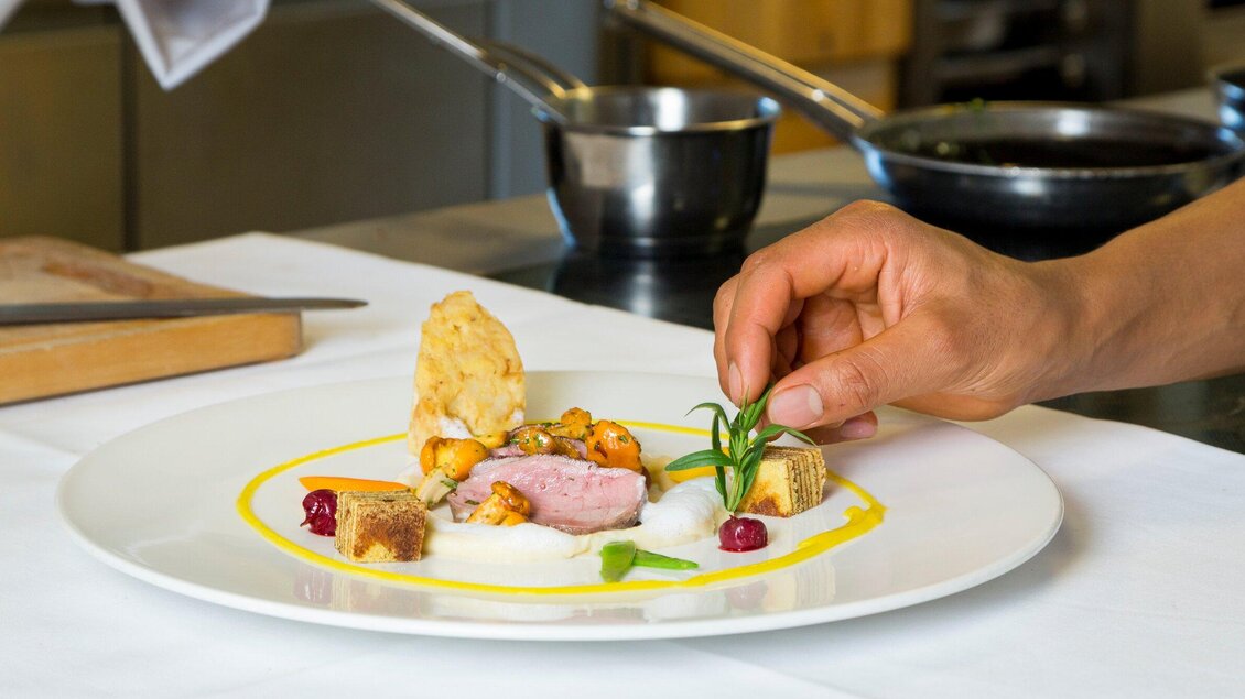 Ein kunstvoll angerichteter Teller mit feinem Fleisch, Gemüse und Saucen. Eine Hand fügt gerade eine Dekoration hinzu. | © TV Region Graz - René Vidalli