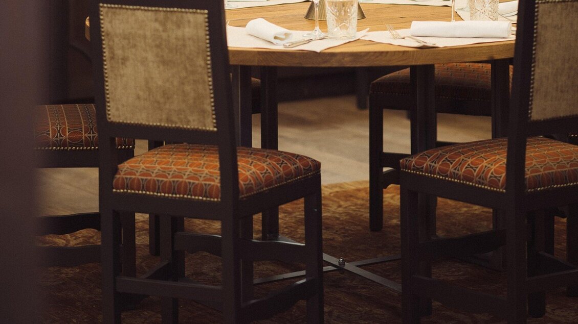 Ein runder Tisch mit rustikaler Holzoptik steht im Mittelpunkt. Rund um den Tisch sind einige stilvolle Stühle mit gepolsterten Sitzen platziert. | © Landhauskeller