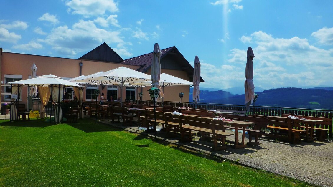 Eine einladende Terrasse mit Sitzplätzen und Sonnenschirmen. Im Hintergrund erstreckt sich eine malerische Landschaft unter einem blauen Himmel. | © Landhotel Reitingblick