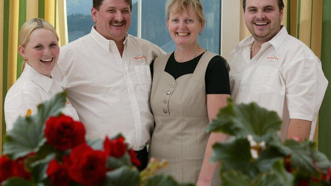 Vier Personen lächeln in einer freundlichen Umgebung. Im Vordergrund sind rote Rosen zu sehen. | © Landhotel Reitingblick