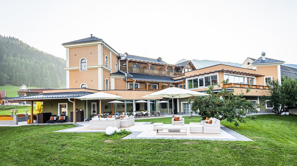 Ein elegantes Hotelgebäude umgeben von einer grünen Wiese und Bergen. Die Terrasse lädt zum Entspannen im Freien ein. | © Landhotel Timmerer