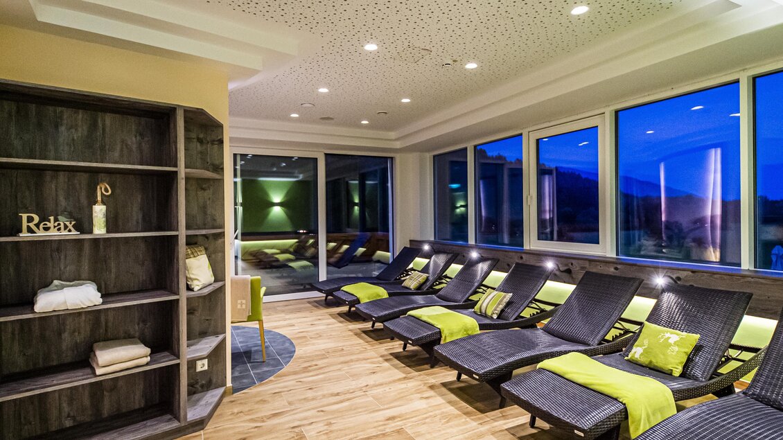 Ein entspannender Wellnessbereich mit gemütlichen Liegen und sanftem Licht. Die großen Fenster bieten einen Blick auf die Dächer der Stadt. | © Landhotel Timmerer