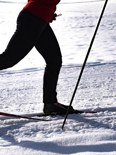 A person cross-country skiing on a snowy surface. The skier is wearing black pants and a red top. | © Erlebnisregion Murtal