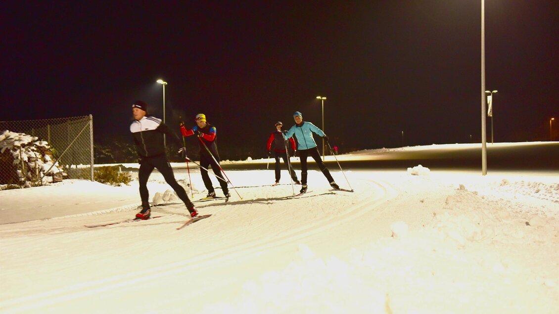 Vier Menschen beim Langlaufen auf einer schneebedeckten Strecke in der Nacht. Die Umgebung ist beleuchtet, und der Schnee reflektiert das Licht. | © Erlebnisregion Murtal