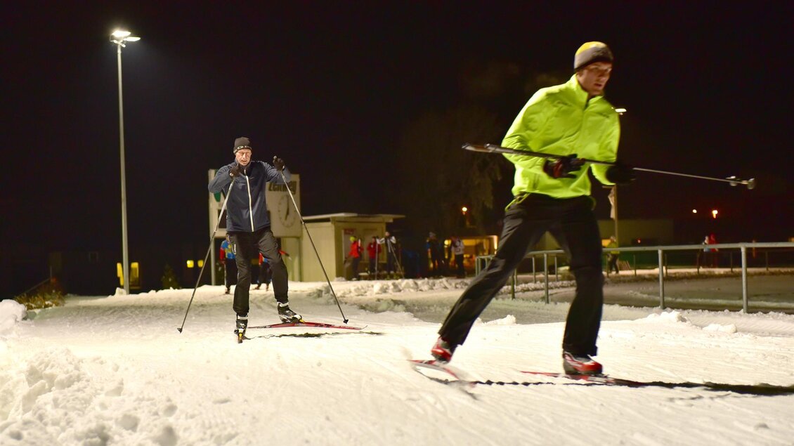 Zwei Männer skifahren in der Nacht auf einer beleuchteten Loipe. Der Mann in gelber Jacke führt die Gruppe an. | © Erlebnisregion Murtal