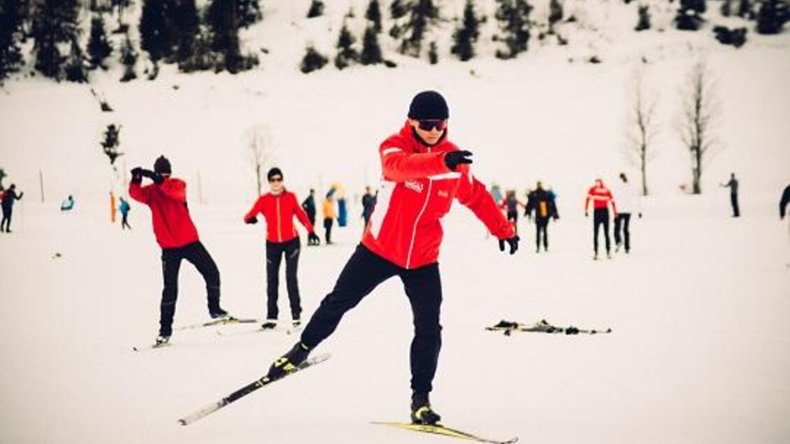 Eine Gruppe von Skifahrern in roten Jacken auf einer verschneiten Fläche. Sie sind aktiv beim Langlaufen und genießen die winterliche Umgebung. | © Langlaufschule Ramsau