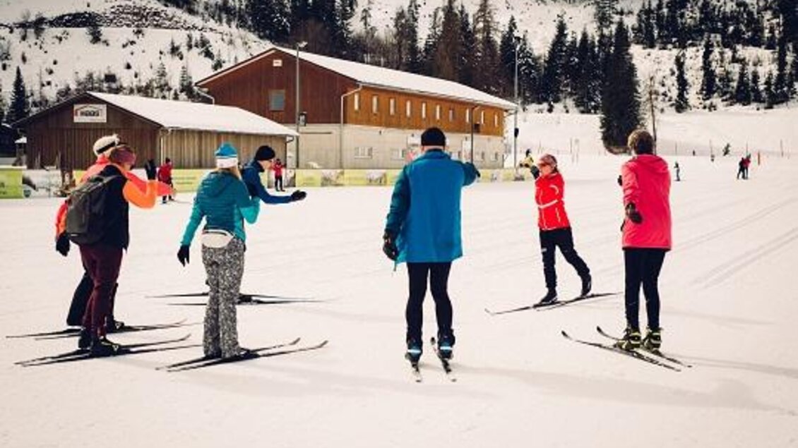 Eine Gruppe von Skifahrern steht auf einer verschneiten Piste. Im Hintergrund sind Hütten und Bäume zu sehen. | © Langlaufschule Ramsau