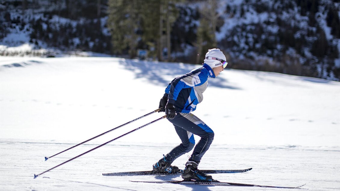 Ein Skifahrer fährt auf einer schneebedeckten Piste. Im Hintergrund sind Bäume und ein klarer Himmel zu sehen. | © Tom Lamm