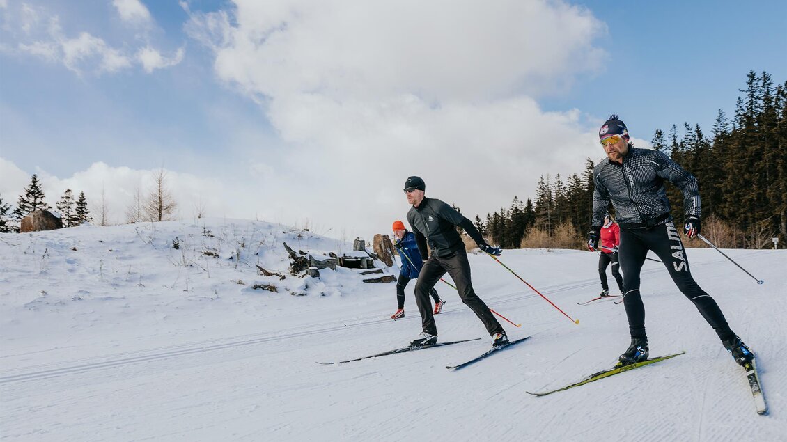 Eine Gruppe von Skifahrern, die auf einer schneebedeckten Strecke unterwegs ist. Im Hintergrund sind Bäume und ein blauer Himmel zu sehen. | © Schilcherland Steiermark