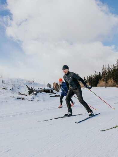 Eine Gruppe von Skifahrern, die auf einer schneebedeckten Strecke unterwegs ist. Im Hintergrund sind Bäume und ein blauer Himmel zu sehen. | © Schilcherland Steiermark