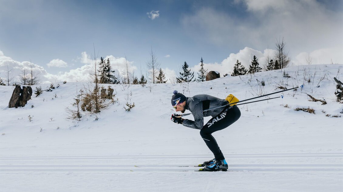 Ein Skifahrer in einer dynamischen Position auf einer verschneiten Strecke. Im Hintergrund sind Bäume und ein klarer Himmel sichtbar. | © Schilcherland Steiermark