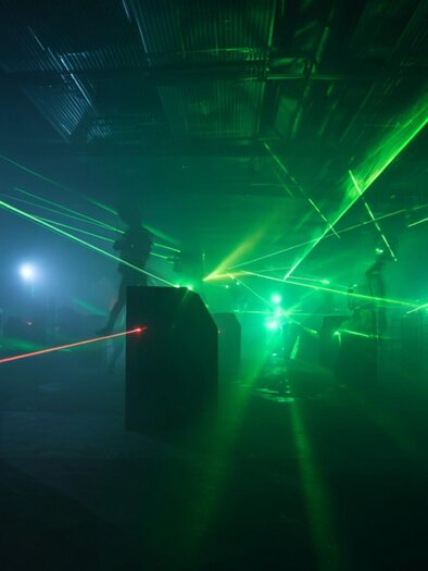 A dimly lit laser tag arena filled with vibrant green and red laser beams cutting through the air. | © Midjourney - Benedikt Trummer