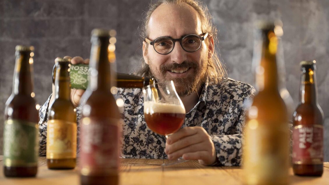 Ein Mann mit Brille gießt Bier in ein Glas. Im Vordergrund sind mehrere Bierflaschen sichtbar. | © Lava Bräu