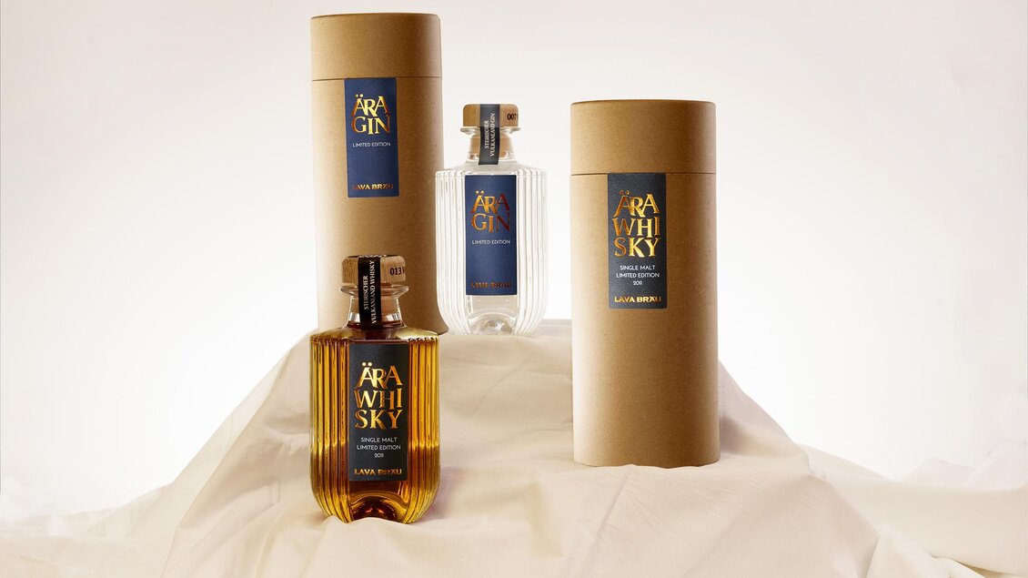 Eine stilvolle Produktpräsentation von Gin und Whisky in eleganten Flaschen und Verpackungen. Die Produkte stehen auf einer weißen Unterlage und verleihen dem Bild eine moderne Note.