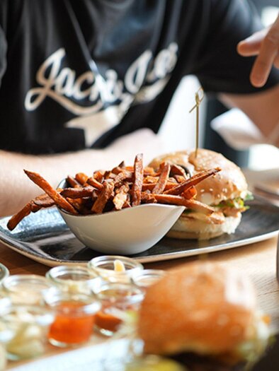 A table with delicious food, including a burger and sweet potato fries. In the background, various side dishes and drinks can be seen. | © Le Burger - The Guardians