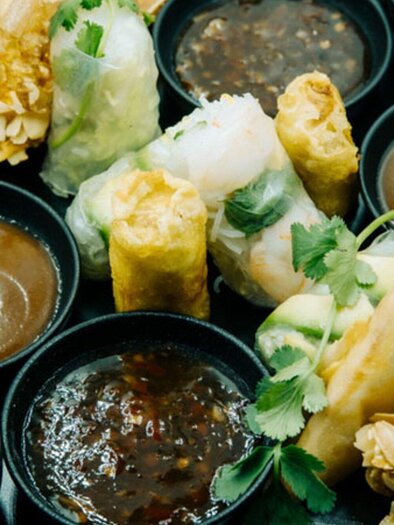 A plate with various Asian snacks, including spring rolls and stuffed dumplings. There are also several bowls with different sauces. | © Le Viet@Graz