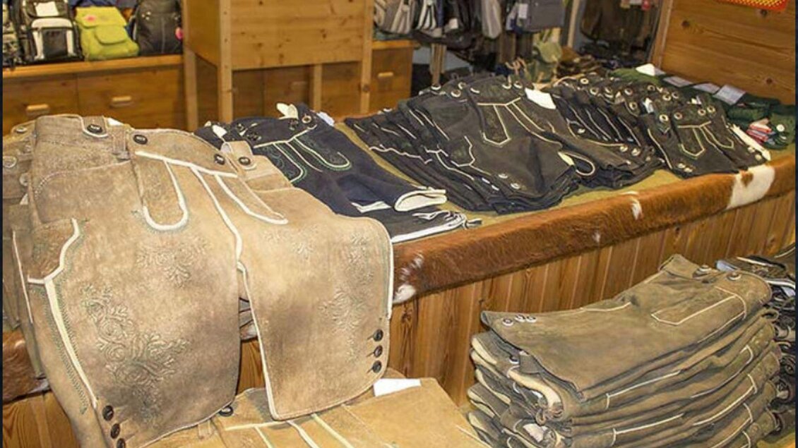 Eine Auswahl an traditioneller Trachtenmode ist auf einem Tisch ausgestellt. Die Hosen sind in verschiedenen Farben und Designs angeordnet. | © Leder Traninger