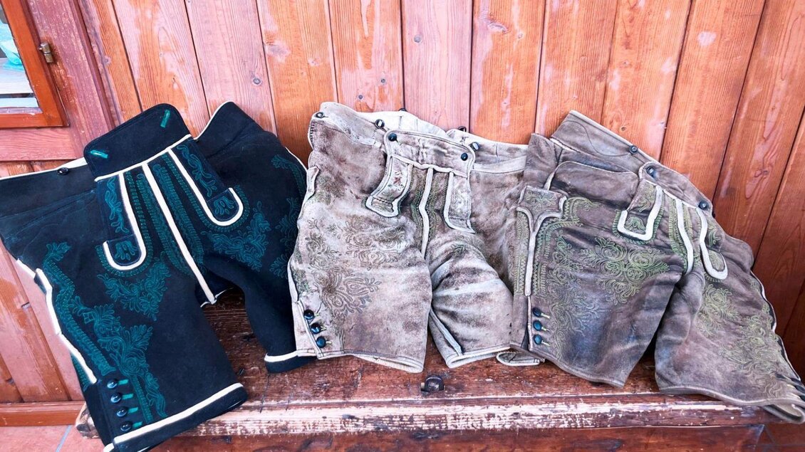 Eine Auswahl von traditionellen Lederhosen in verschiedenen Farben und Designs. Sie sind auf einer Holzoberfläche angeordnet. | © Christian Raich