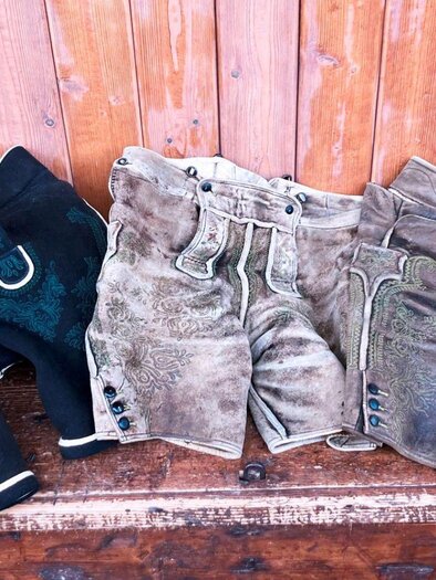A selection of traditional lederhosen in various colors and designs. They are arranged on a wooden surface. | © Christian Raich