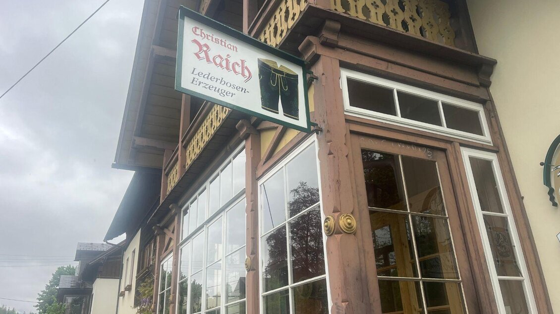 Ein traditionelles Gebäude mit einem einladenden Schild, das die Lederwaren von Raich bewirbt. Die Fensterfront zeigt einen Blick nach draußen, während die Wolken den Himmel dunkel erscheinen lassen. | © TVB Ausseerland Salzkammergut_ Nathalie Schickinger