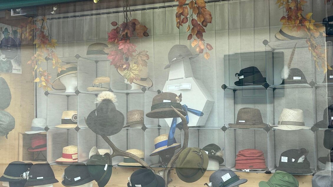 Eine Schaufensterdekoration mit vielen verschiedenen Hüten in verschiedenen Stilen und Farben. Herbstliche Blätter verleihen dem Bild eine gemütliche Atmosphäre. | © TVB Ausseerland Salzkammergut_ Nathalie Schröttenhamer