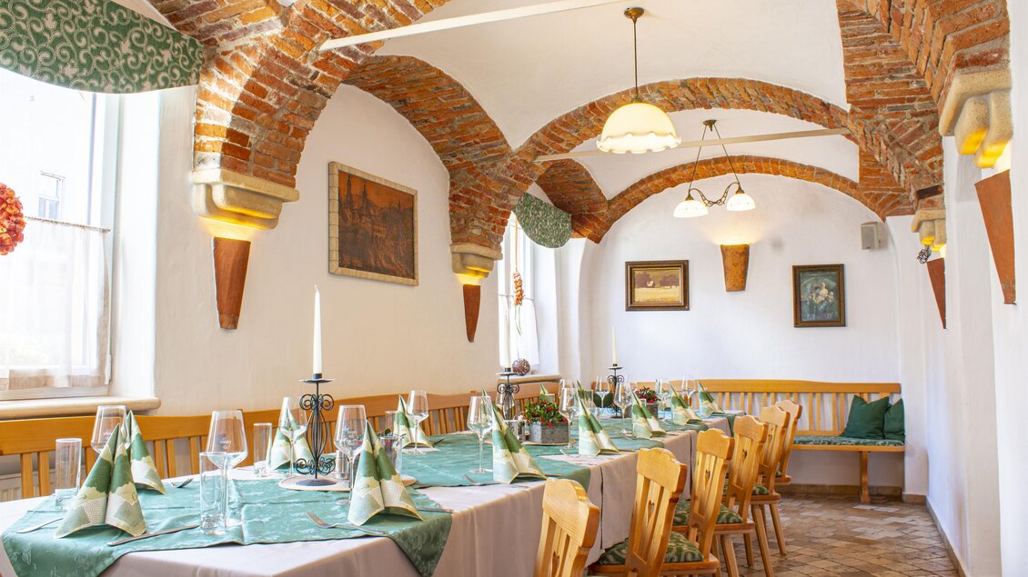 Ein einladender Speisesaal mit einem langen Tisch, gedeckt mit grünen Servietten. Die Decke ist mit Ziegelsteinen und dekorativen Lampen gestaltet. | © Lendplatzl