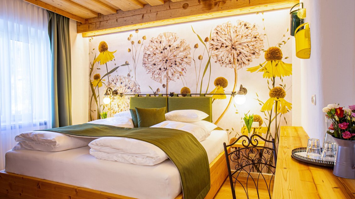 Ein helles und gemütliches Schlafzimmer mit einem Doppelbett und frischen Blumenmotiven an der Wand. Holzmöbel und sanfte Farben schaffen eine einladende Atmosphäre. | © Lendplatzl