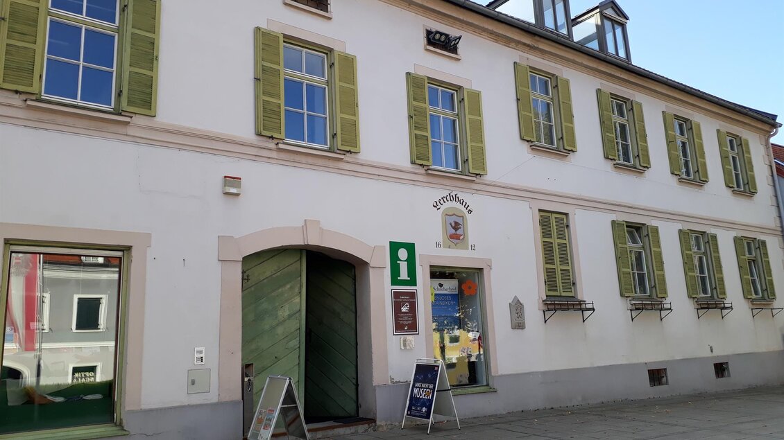 Ein historisches Gebäude mit einer weißen Fassade und grünen Fensterläden. Vor dem Gebäude stehen Informationsschilder und Tische. | © Schilcherland Steiermark