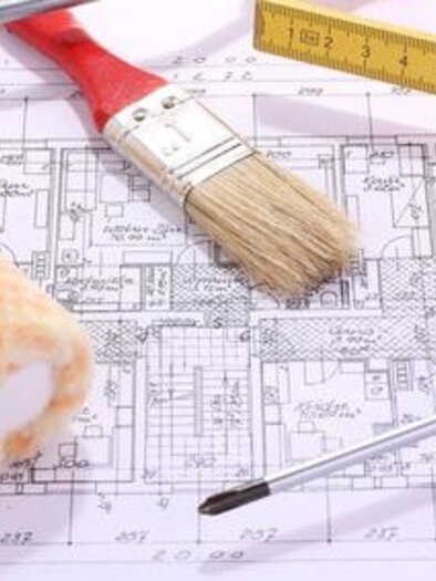 A blueprint is lying on a table, surrounded by tools like a brush, a paint roller, and a screwdriver. These objects suggest renovation or construction work. | © Symbolfoto Fotolia