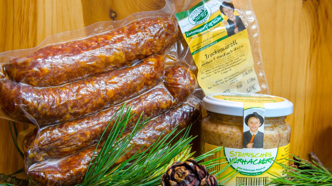 Eine Packung mit Wurst und ein Glas Senf stehen auf einem Holzuntergrund. Neben dem Essen liegen einige Tannenzweige und ein Tannenzapfen. | © Erlebnisregion Murtal