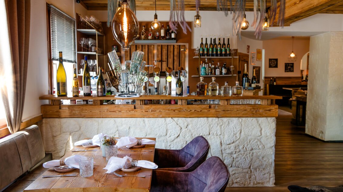 Ein stilvolles Restaurant mit einer Holzbar und modernen Beleuchtungselementen. Der Tisch ist elegant gedeckt und einladend. | © Region Graz - Mias Photoart