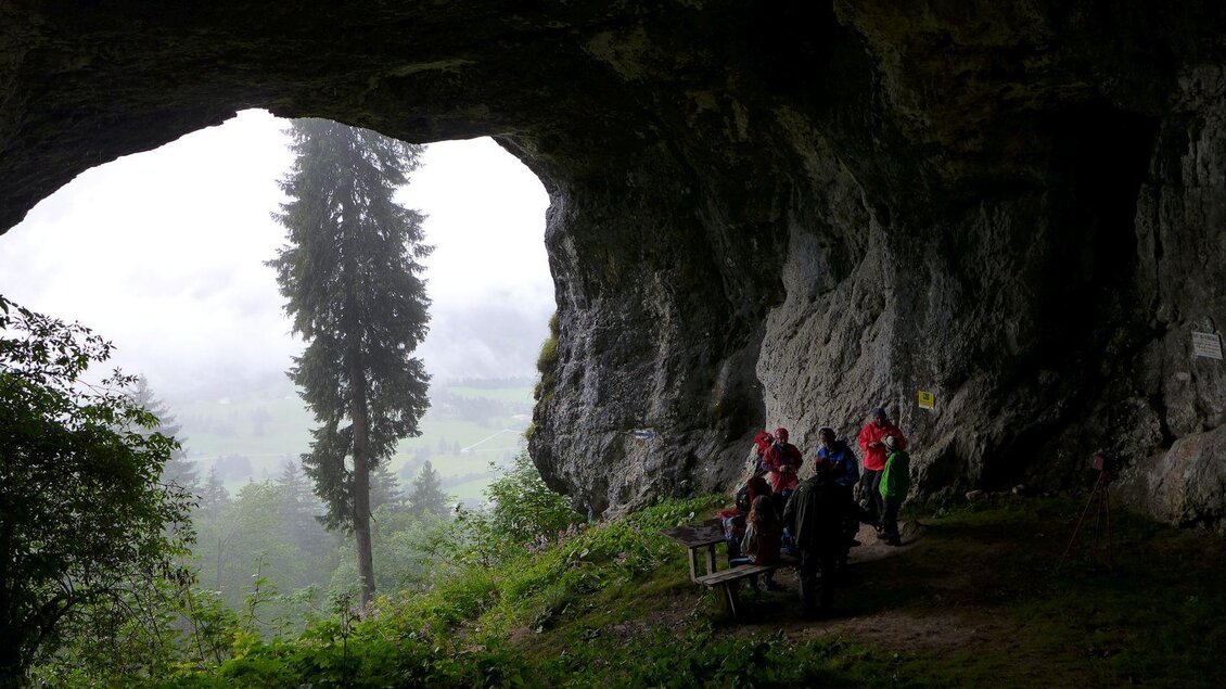 Eine Höhle mit Blick auf eine neblige Landschaft. Einige Wanderer sitzen auf einer Bank und genießen die Aussicht. | © Robert Seebacher