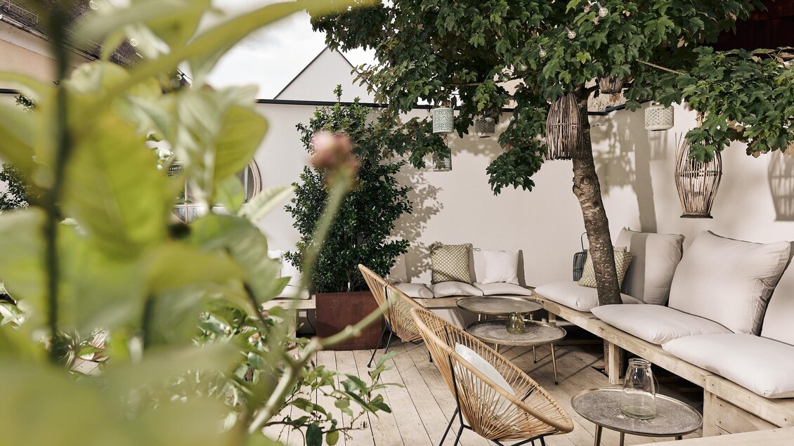 Eine gemütliche Terrasse mit bequemen Sitzgelegenheiten und einem Tisch. Grüne Pflanzen sorgen für eine entspannte Atmosphäre.