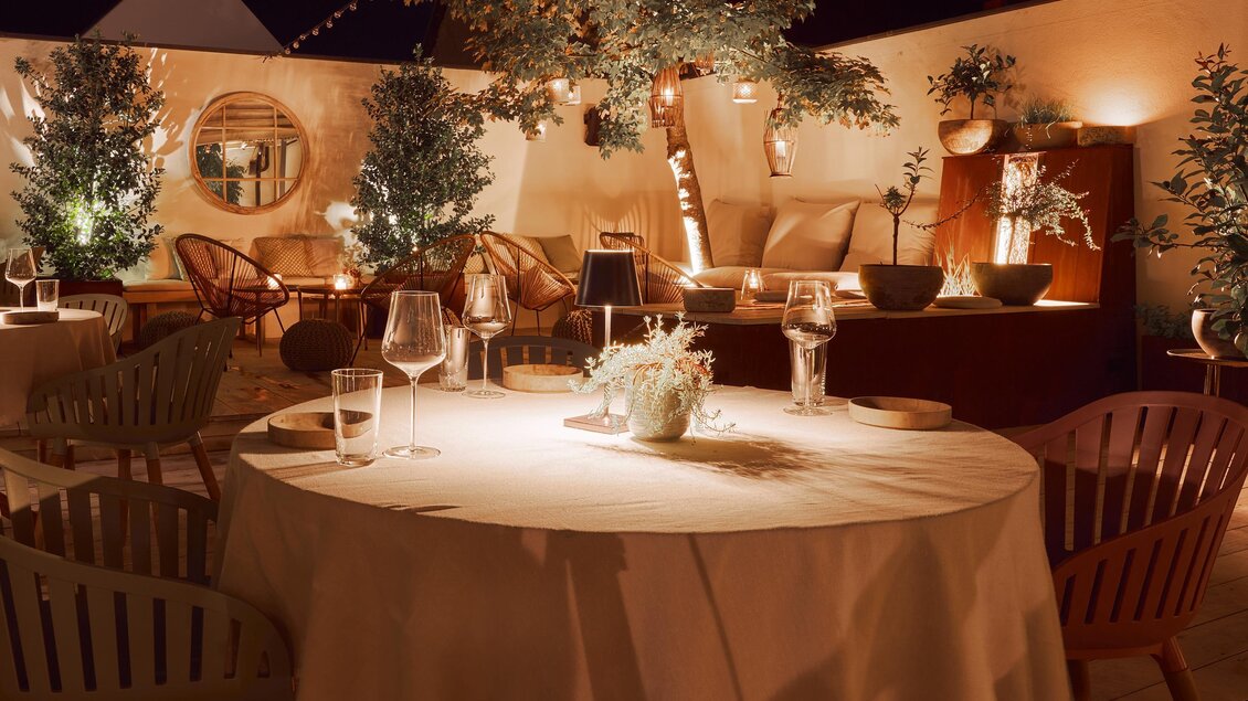 Ein elegantes Restaurant mit sanfter Beleuchtung und gemütlichen Sitzbereichen. Tische sind festlich gedeckt und Pflanzen sorgen für eine entspannte Atmosphäre.