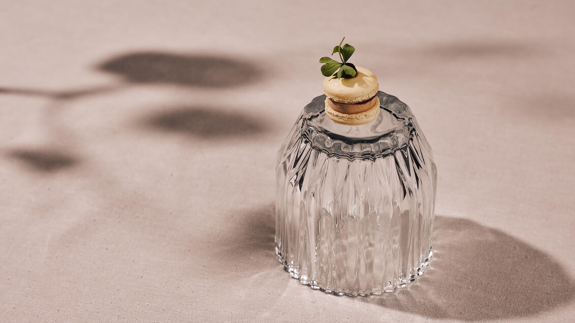 Ein dekoratives Glasgefäß mit einem Korken und einer kleinen Pflanze oben drauf. Der Hintergrund ist neutral und hebt das Gefäß hervor.