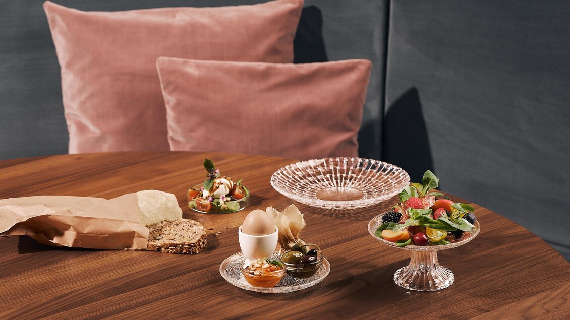 Ein schön gedeckter Tisch mit verschiedenen Gerichten und Desserts. Im Hintergrund sind weiche, rosa Kissen sichtbar.