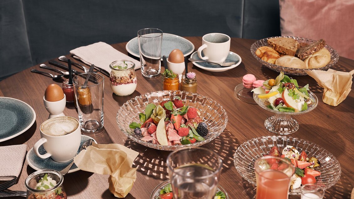 Ein schön gedeckter Tisch mit verschiedenen Köstlichkeiten, darunter Salate, Fleischgerichte und Gebäck. Dazu stehen Getränke in Gläsern und Tassen bereit.