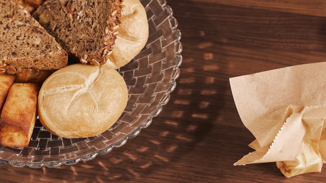 Eine Auswahl an frischem Brot und Brötchen auf einem Glasplatten. Daneben liegt ein Stück Papier.
