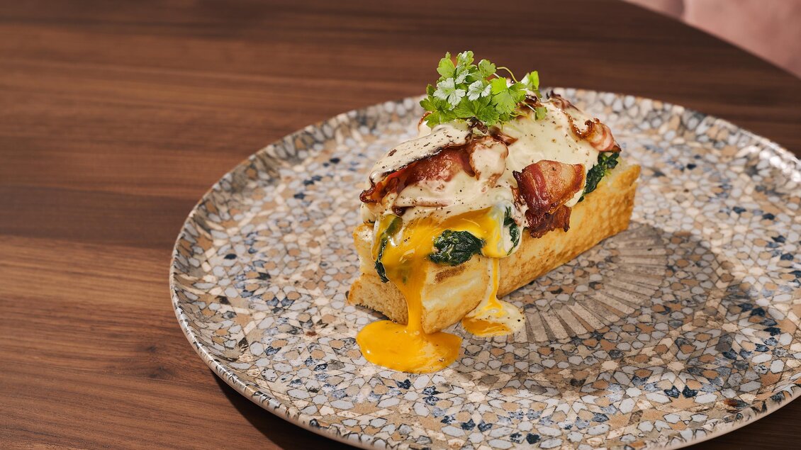 Ein köstliches Gericht auf einem dekorativen Teller. Es zeigt eine Scheibe Brot mit Spinat, Schinken und einem weichgekochten Ei.