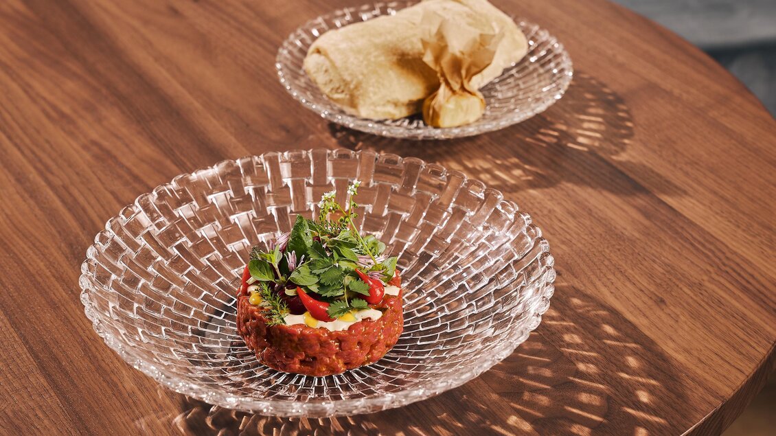Ein eleganter Teller mit einem bunten, frisch zubereiteten Salat und einer schmackhaften Sauce liegt auf einem holzfarbenen Tisch. Nebenbei ein weiterer Teller mit knusprigen Chips.