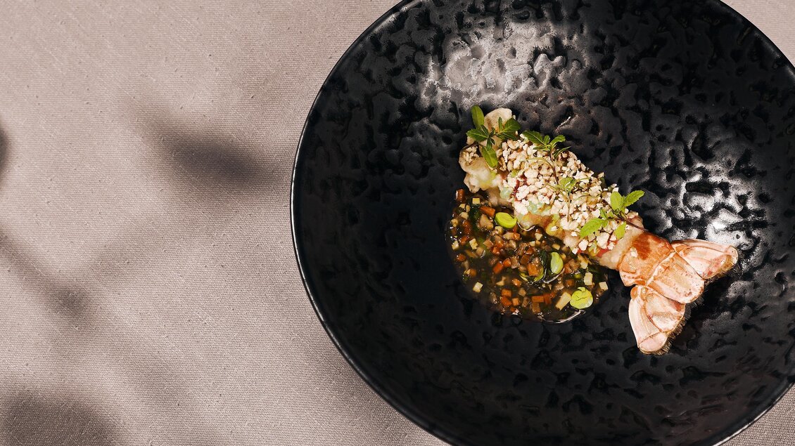 Ein kunstvoll angerichteter Teller mit einer Garnelenspeise und bunten Zutaten. Die dunkle Schüssel hebt die visuellen Elemente hervor.