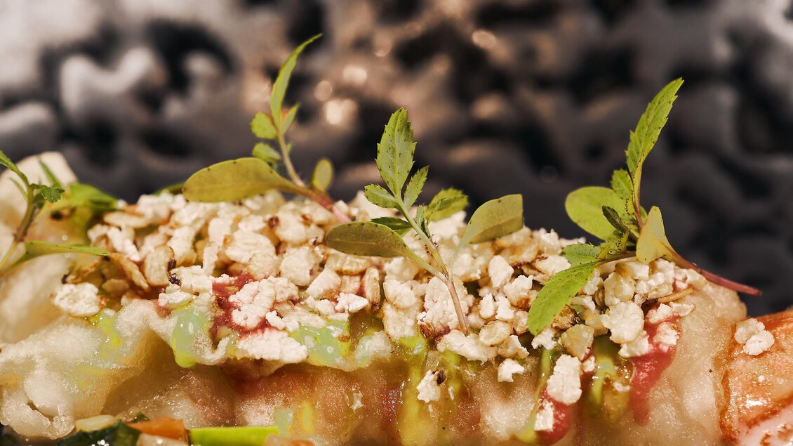 Ein köstlicher Burrito mit frischem Gemüse und einer knackigen Topping aus Nüssen. Im Hintergrund ist eine dunkle, unscharfe Textur zu sehen.