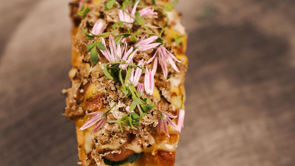 Ein köstliches Gericht auf einem Holzbrett, belegt mit zarten Fleischstücken und bunten essbaren Blumen. Das Essen sieht sehr ansprechend und frisch aus.