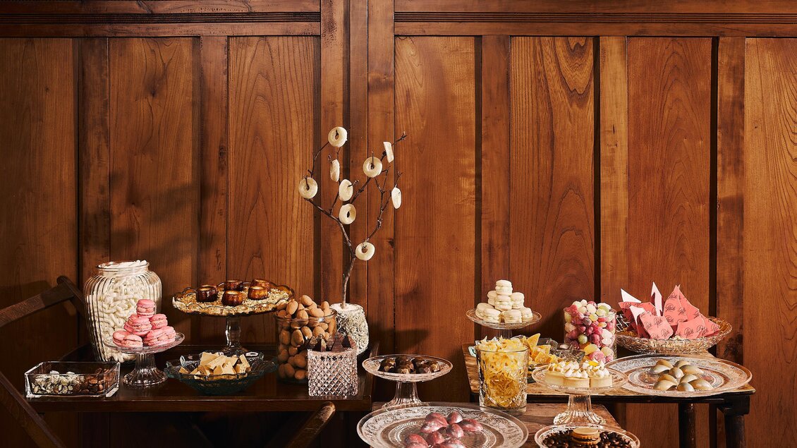 Ein wunderschöner Tisch mit verschiedenen Süßigkeiten und Backwaren. Im Hintergrund sind Holzpaneele zu sehen, die eine gemütliche Atmosphäre schaffen.